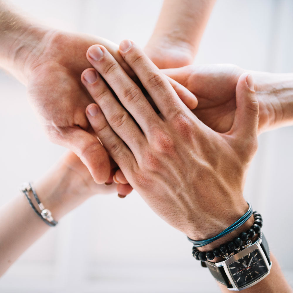 cover image for an article listing some of the best cooperative board games, picture depicts five hands put together representing cooperation