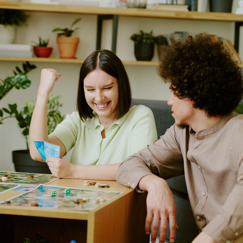 a couple playing a two player baord game, the woman is winning and excited